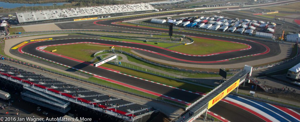 Aerial view of a Formula 1 racetrack with winding turns, grandstands, pit buildings, and spectator areas under clear skies.