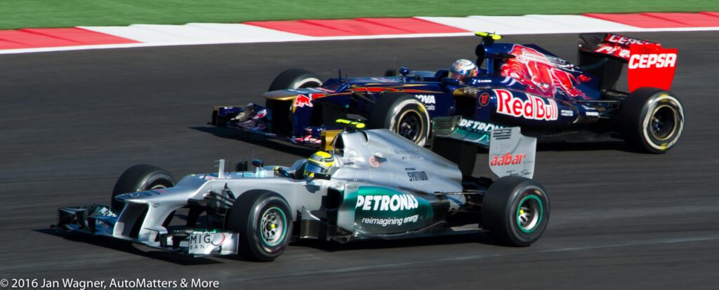 Two Formula 1 cars, one from Mercedes and one from Toro Rosso, race side by side on a track during a competition.