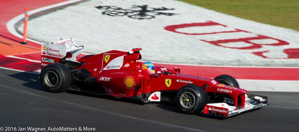 A red Ferrari Formula 1 car races on a track near a UBS logo painted on the grass.
