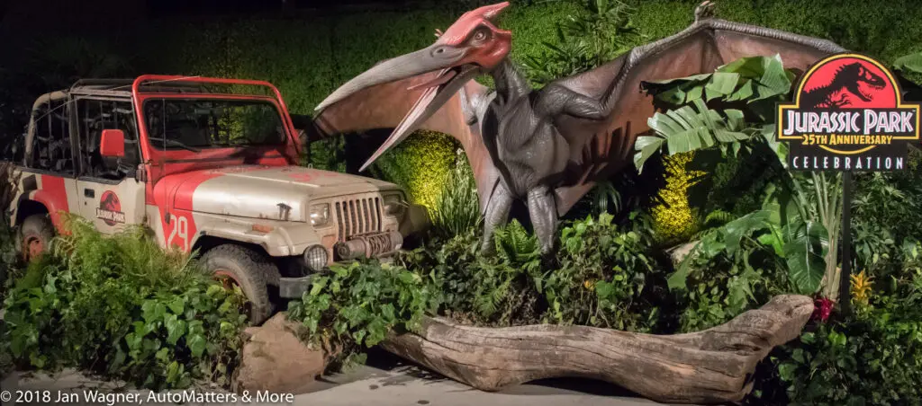 A Jurassic Park 25th Anniversary display featuring a model of a pterosaur, a Jurassic Park-branded Jeep, and themed foliage.