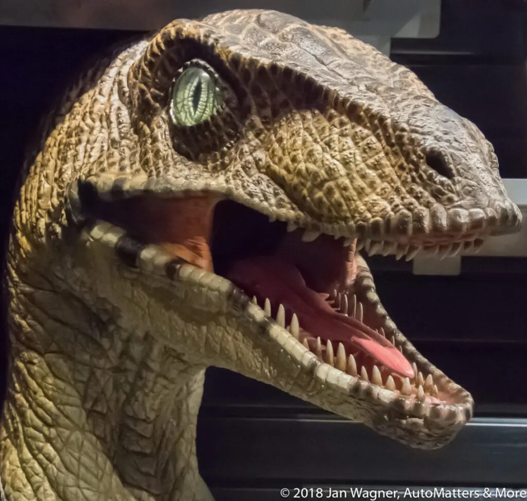 A realistic model of a velociraptor dinosaur with its mouth open, showing sharp teeth and detailed skin texture.