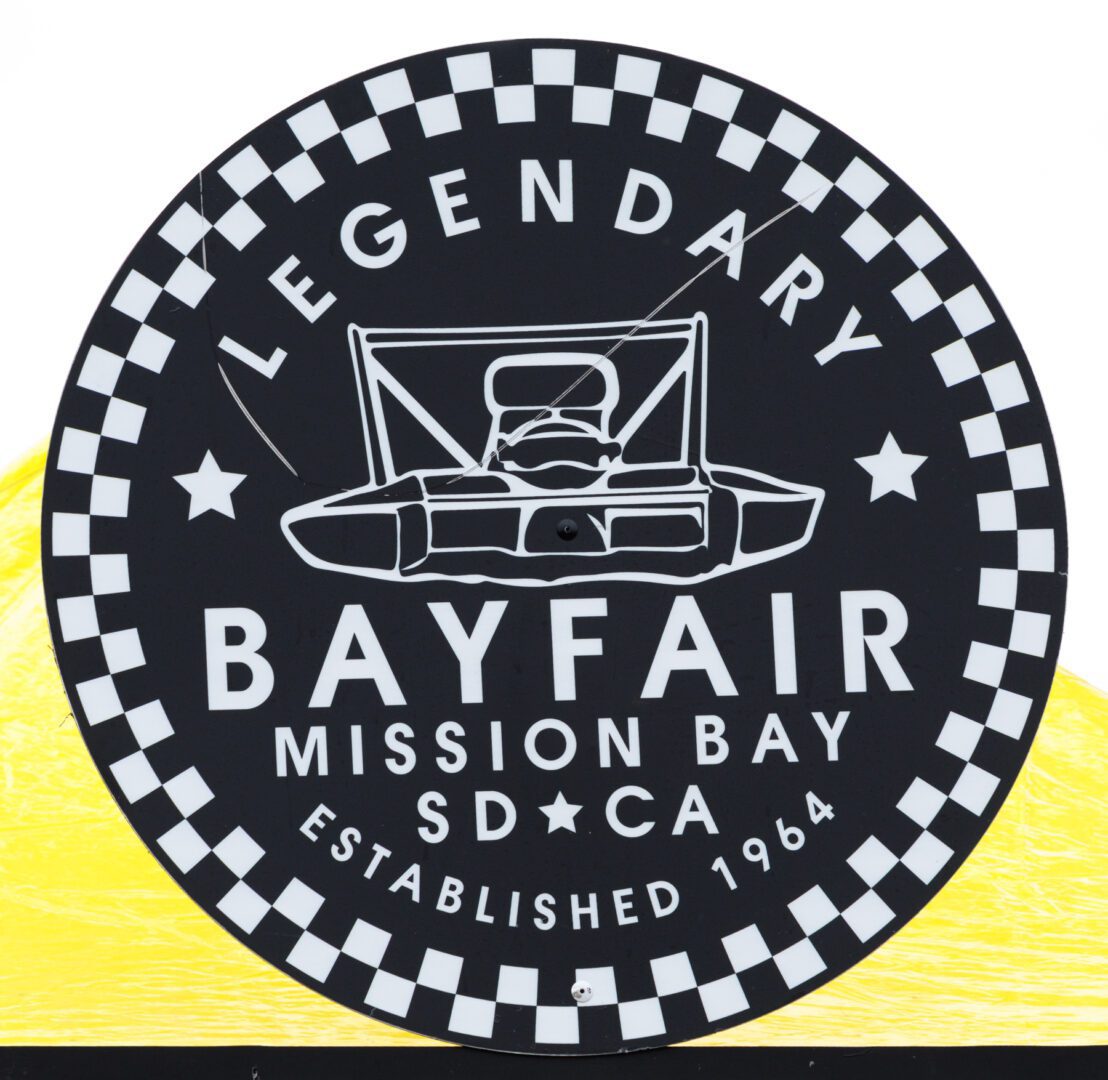 Black and white circular sign reads "Legendary Bayfair Mission Bay SD CA Established 1964" with a drawing of a hydroplane boat in the center and a checkered border.