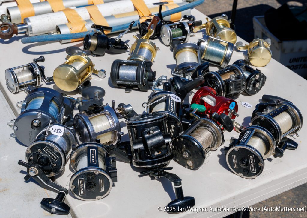 A collection of various fishing reels with lines attached, laid out on a white table at an outdoor setting.