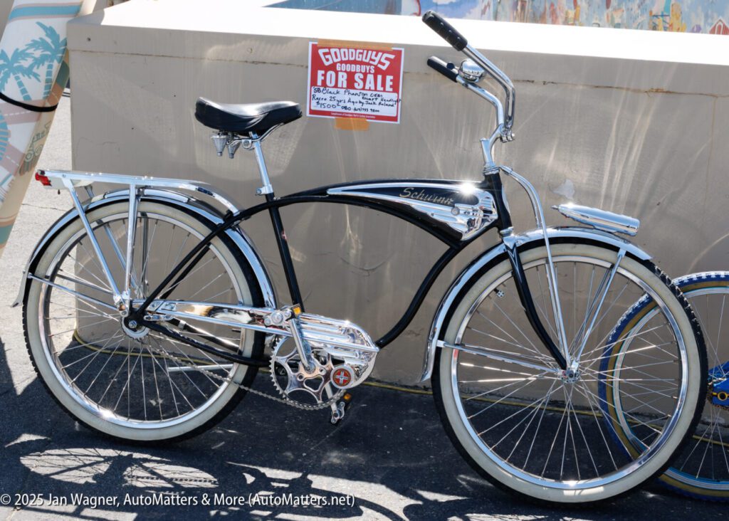 A black and chrome Schwinn bicycle is parked in front of a wall, with a "For Sale" sign displayed above it.
