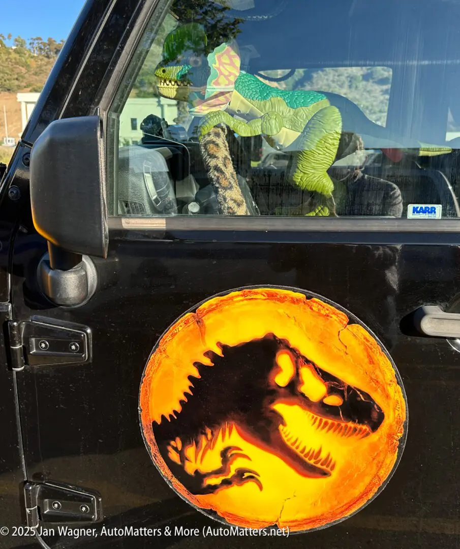 Plastic dinosaur toys are displayed inside a car, which has a large Jurassic Park-style dinosaur logo on its black door.