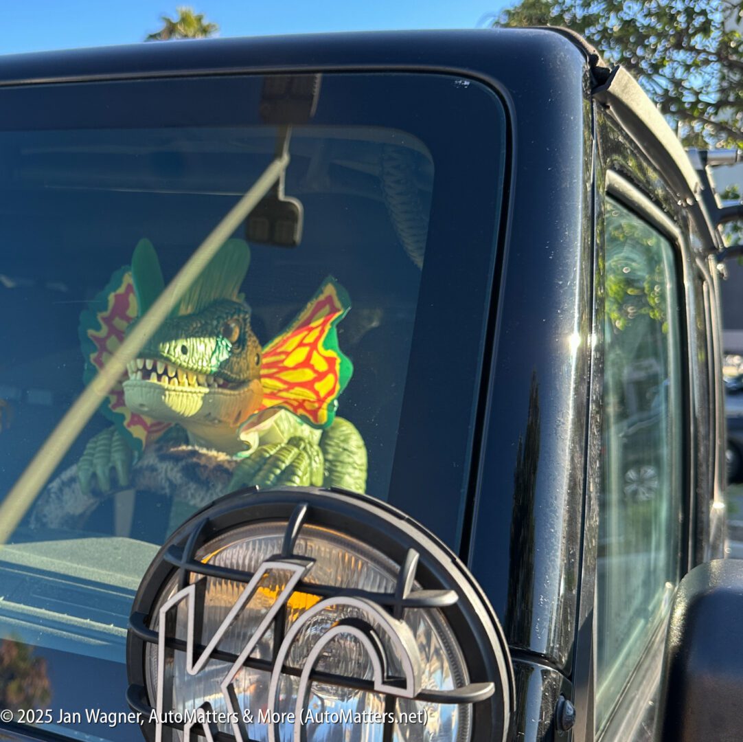A toy dinosaur with colorful frills is placed inside a parked vehicle, visible through the front windshield beside the driver's seat.