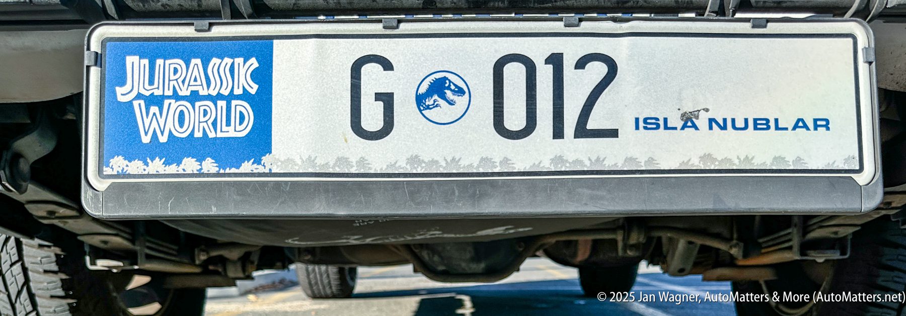 A close-up of a novelty license plate reading "Jurassic World G 012 Isla Nublar" attached to a vehicle.