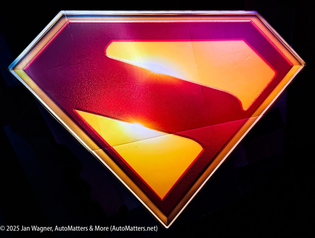 A close-up of a red and yellow Superman logo with a textured surface, illuminated against a dark background.
