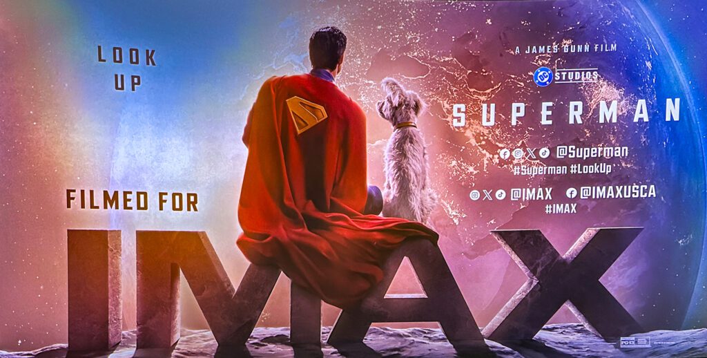 Superman and a dog sit on a ledge overlooking Earth from space, with text promoting the IMAX release of a Superman film.