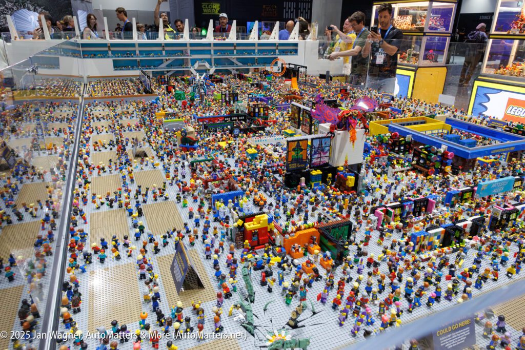 A large, detailed LEGO city display features hundreds of LEGO minifigures and buildings, with people observing behind a glass barrier.