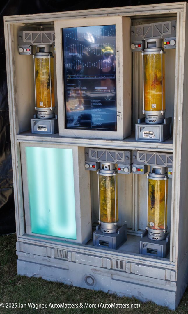 A display case featuring five cylindrical tanks with yellowish contents and a large screen above them, showing technical data and diagrams.