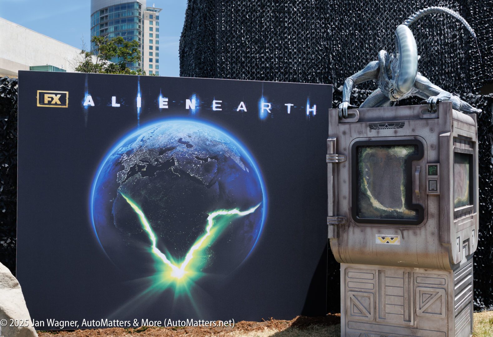 A display for FX's "Alien Earth" features a poster of Earth with a glowing V-shaped light and a model of an alien creature climbing on a sci-fi structure.