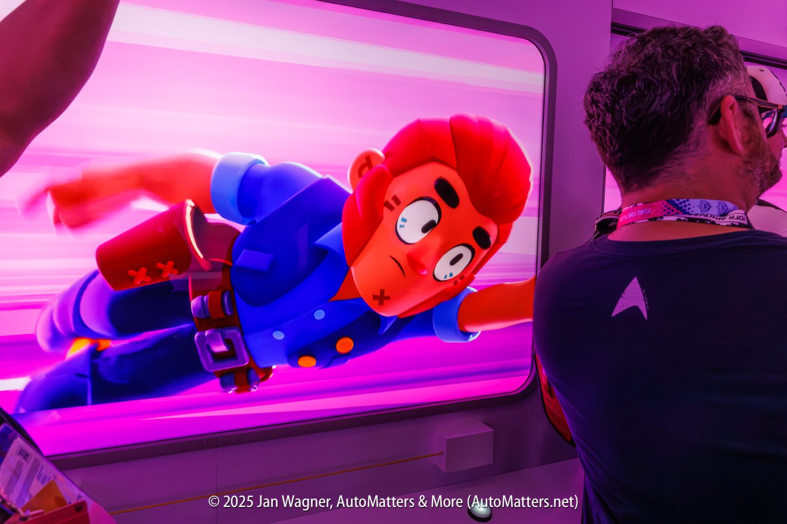 A person stands in front of a large, brightly lit display featuring a cartoon character in blue clothing flying with a determined expression.