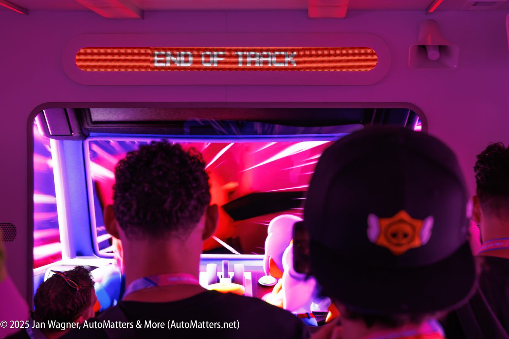 People are seated inside a theme park ride vehicle, facing a screen that displays "END OF TRACK" in red letters.