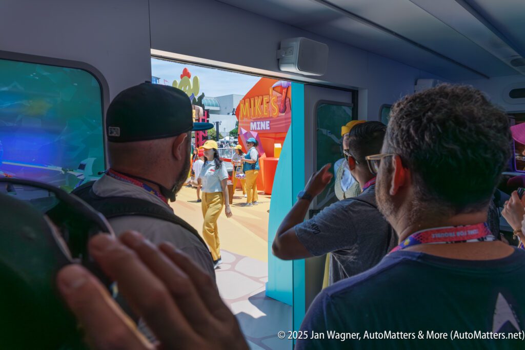 People stand inside a doorway, looking out at a themed outdoor area with colorful decorations and a "MIKE'S MINE" sign.