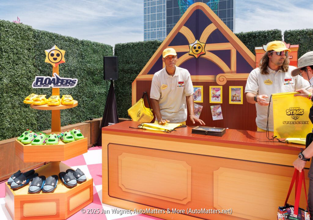 Two people stand behind a themed booth with "Floaters" branded merchandise, including hats, bags, and frog-themed clogs, at an outdoor event.
