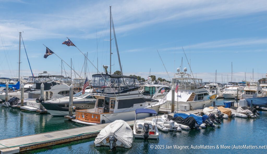 Boats and yachts docked at a marina, with some covered by tarps. Clear sky with scattered clouds in the background.