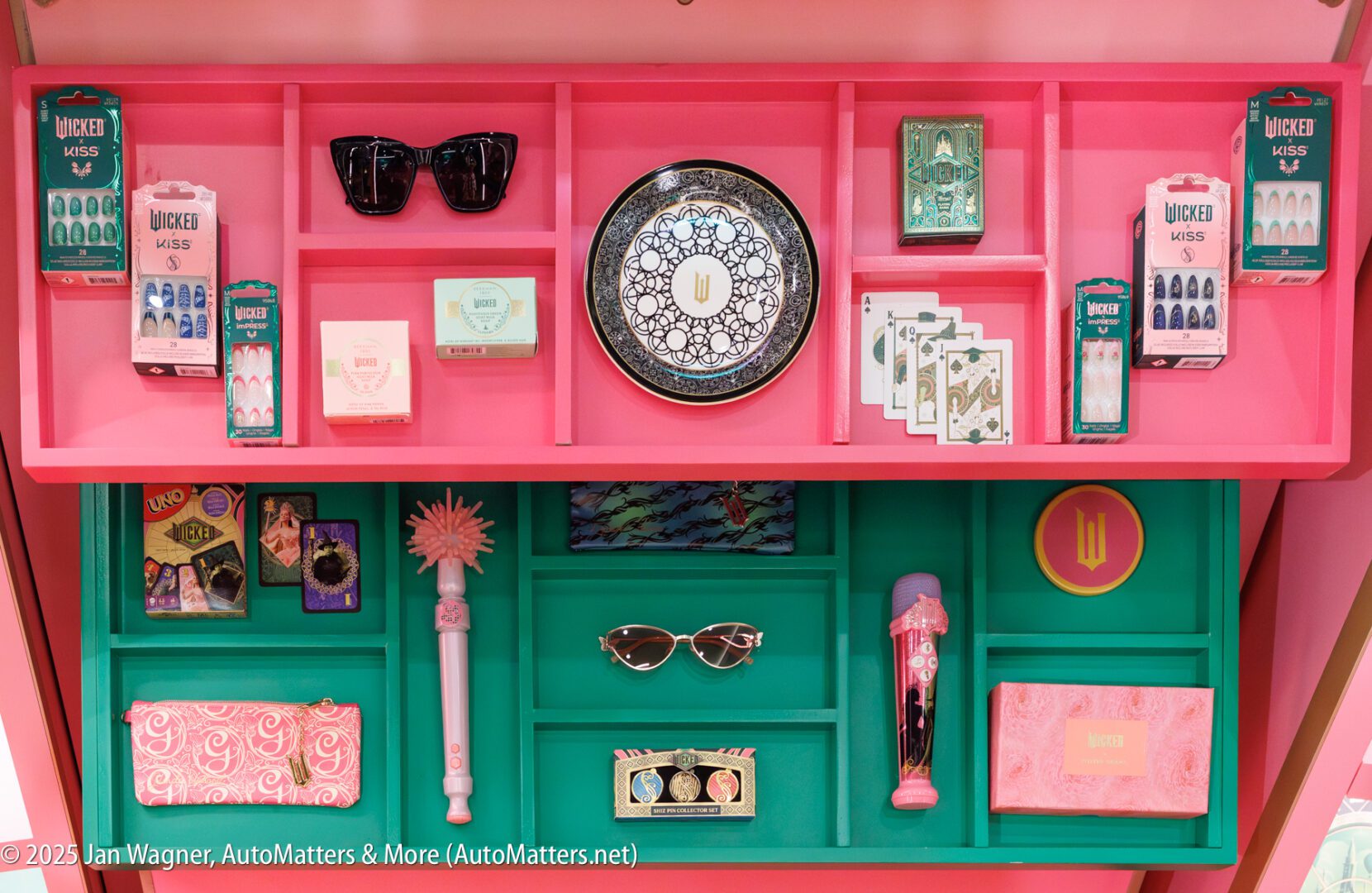 A display case with shelves organizes sunglasses, nail sets, a decorative plate, playing cards, a pen, a wand, and other small accessories in pink and teal compartments.