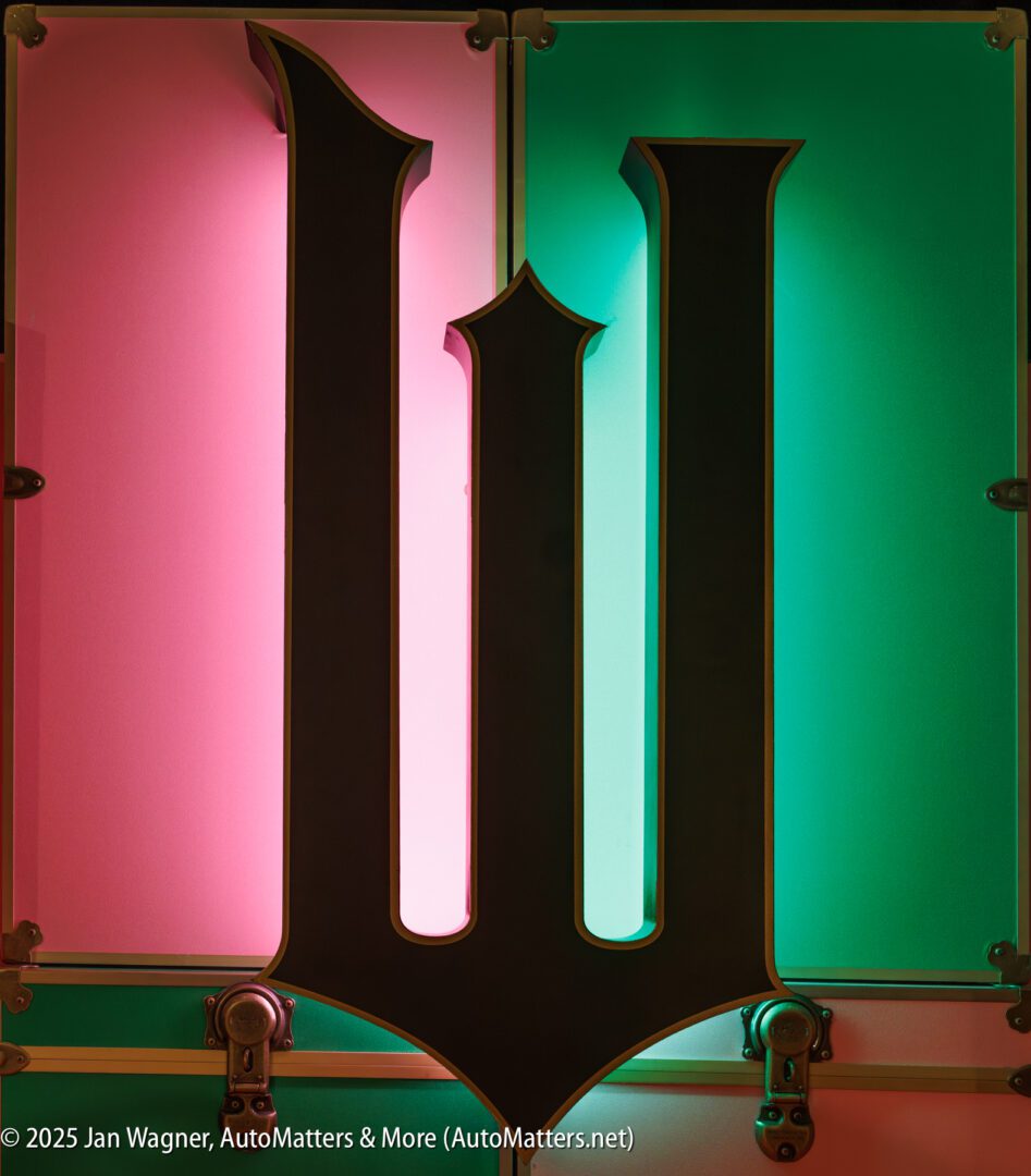 A large, stylized black letter "W" is mounted on a wall, illuminated by pink light on the left and green light on the right.