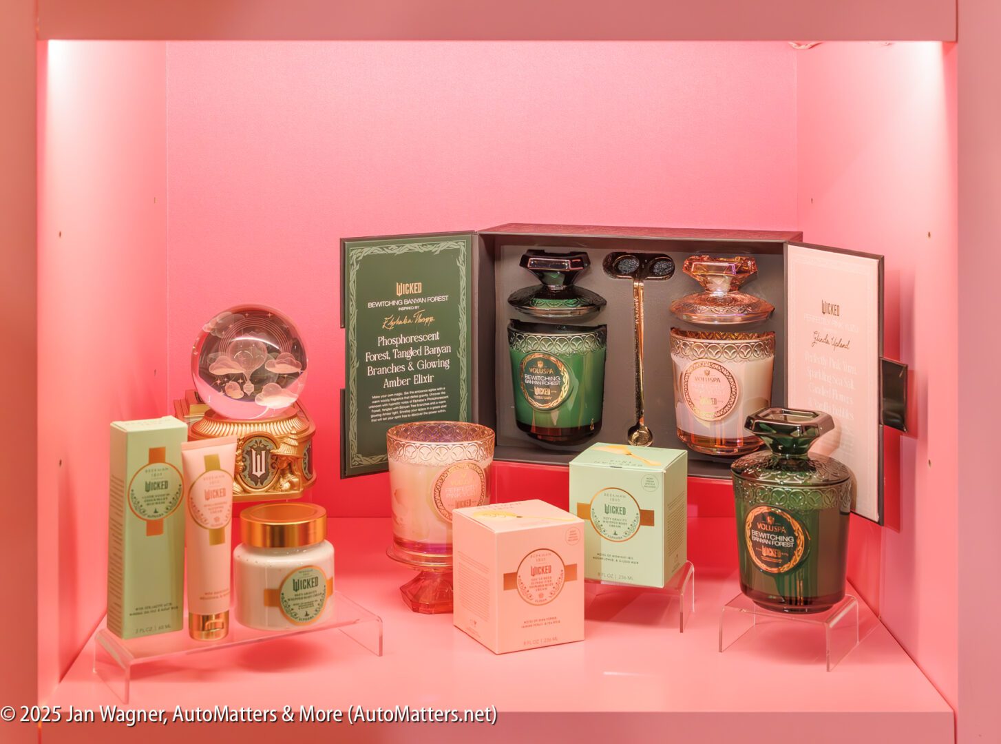 A collection of luxury personal care products, candles, and shaving accessories is displayed on pink shelves with decorative packaging and informational cards.