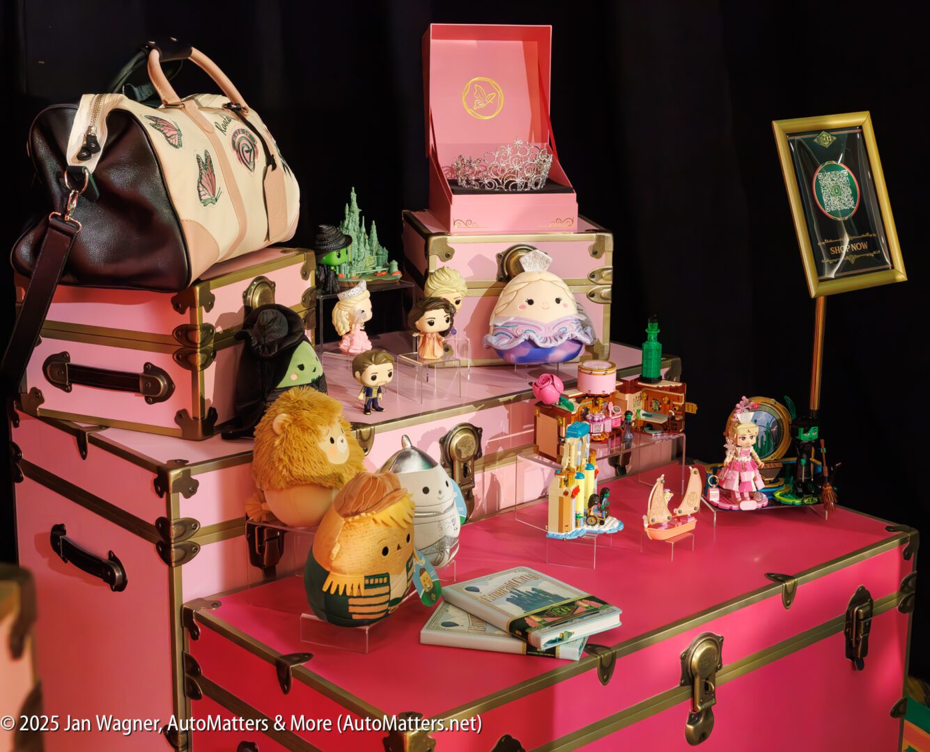 A collection of Disney-themed figurines and toys displayed on stacked pink and cream trunks, with a handbag and accessories arranged around them.