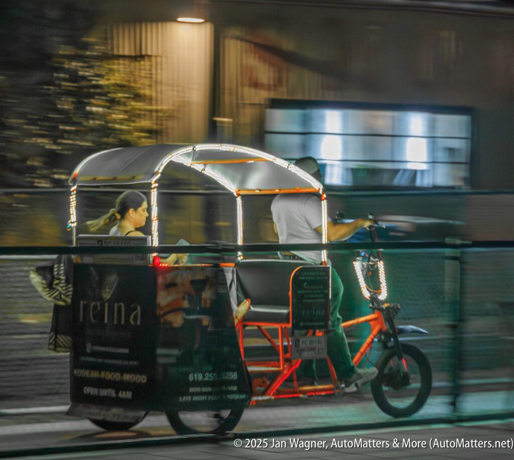 A pedicab decorated with lights carries two passengers at night, moving quickly past a blurred urban background.