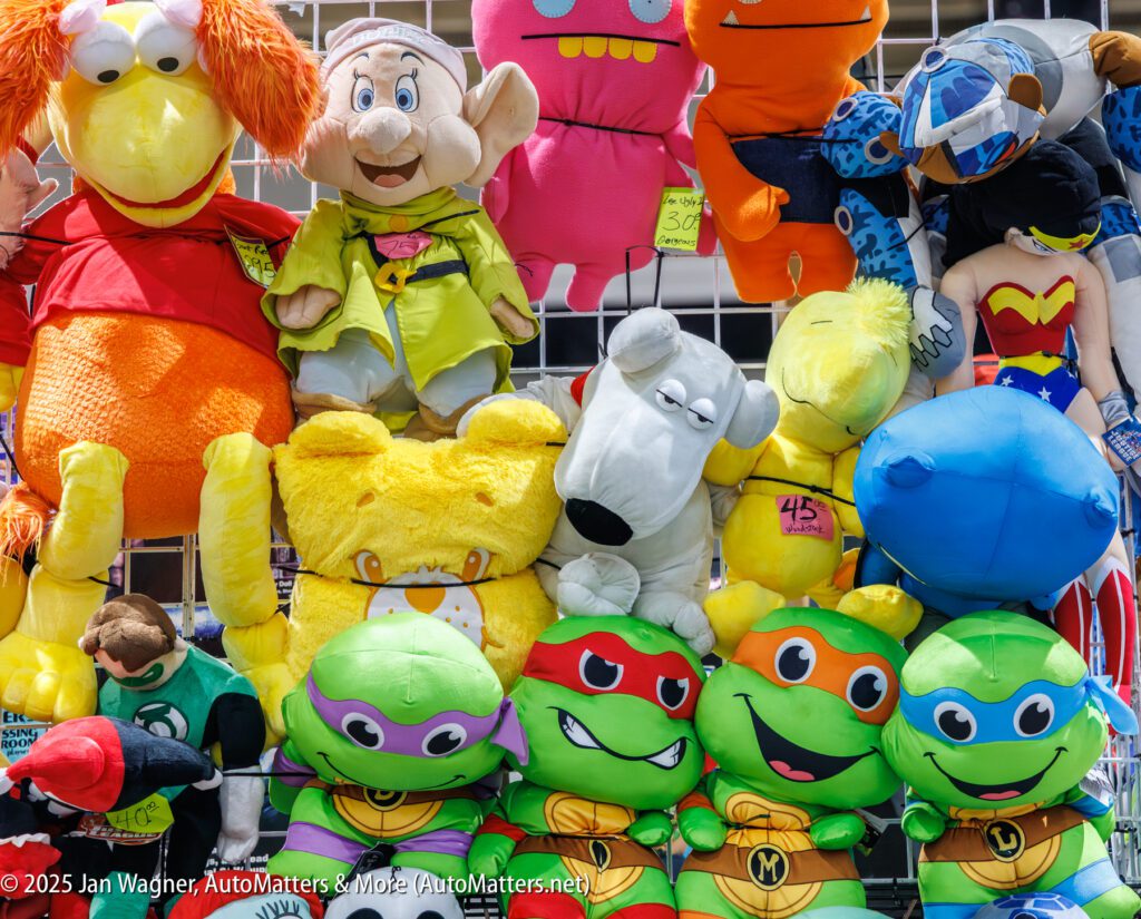 A display of various colorful plush toys featuring cartoon and comic characters arranged on a wire grid at a store or booth.