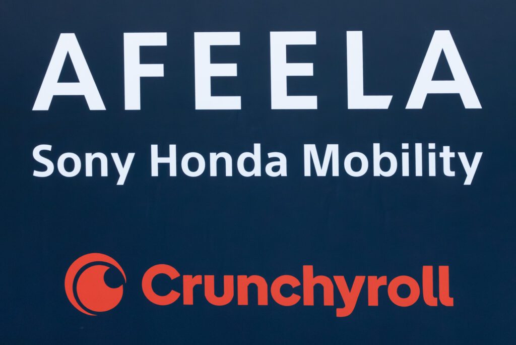 A sign displays the logos and names of AFEELA, Sony Honda Mobility, and Crunchyroll on a dark background.