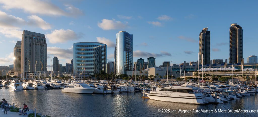 A marina with several docked boats in the foreground and modern high-rise buildings in the background under a partly cloudy sky.