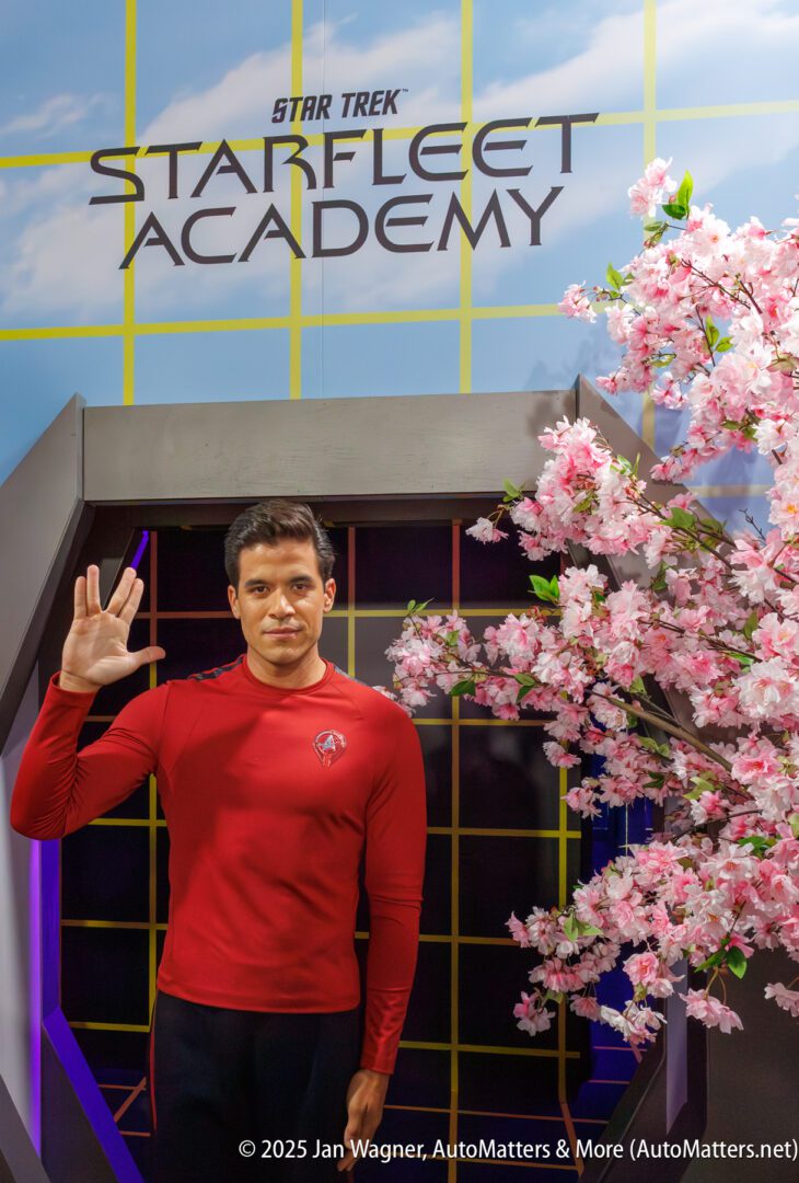 A person in a red Starfleet uniform stands in front of a "Star Trek: Starfleet Academy" sign, giving the Vulcan salute beside a pink flowering tree.