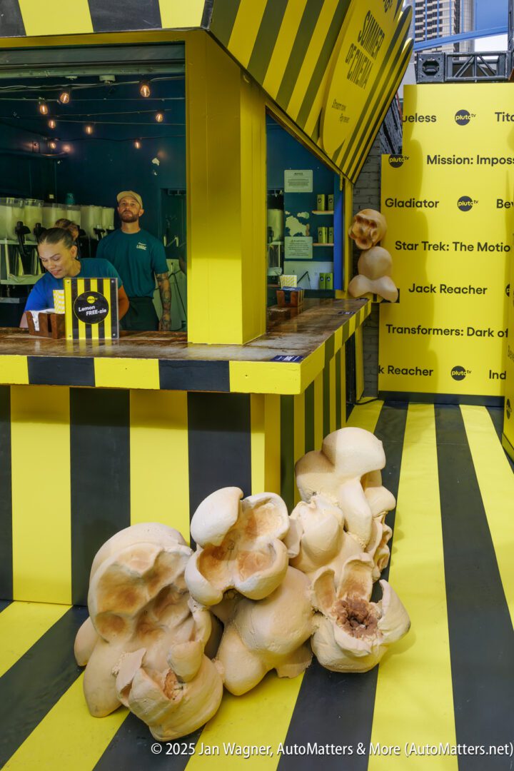 A yellow and black striped booth displays popcorn and film titles, with large popcorn sculptures arranged on the ground and counter. Two staff members stand behind the counter.