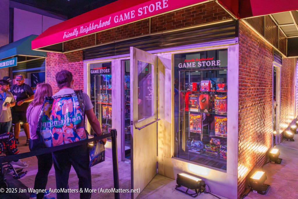 People stand outside a "Friendly Neighborhood Game Store" with open doors, displays of board games in the windows, and a red canopy overhead.