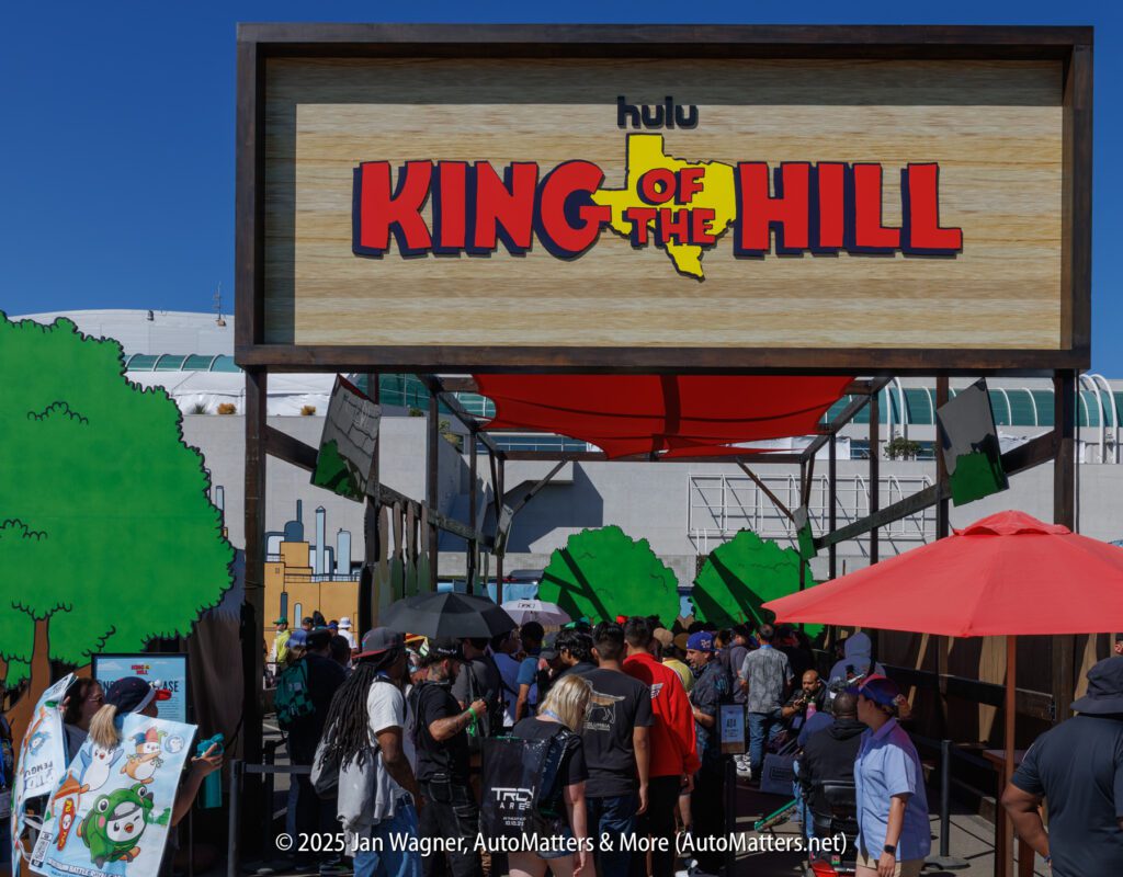 A crowd gathers under a "King of the Hill" sign at a Hulu event with cartoon-themed decorations and umbrellas, likely at a convention.