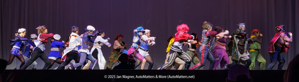 A group of cosplayers in colorful costumes are engaged in a mock battle on stage, facing each other in two distinct lines.