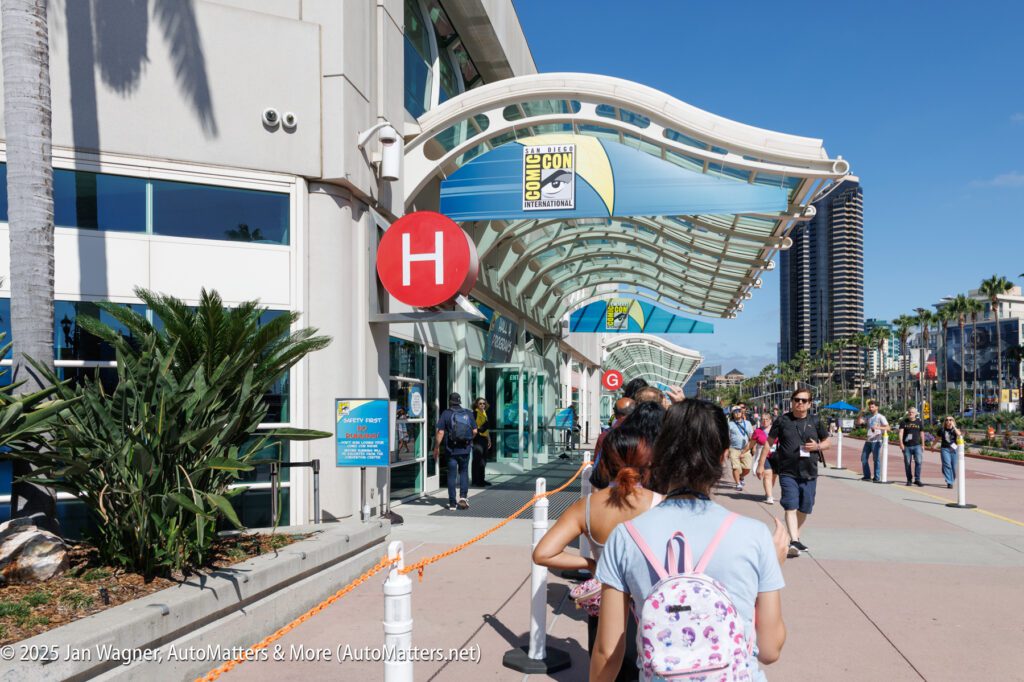 People walk outside the San Diego Convention Center under sunny skies, with Comic-Con signage visible above the entrance.