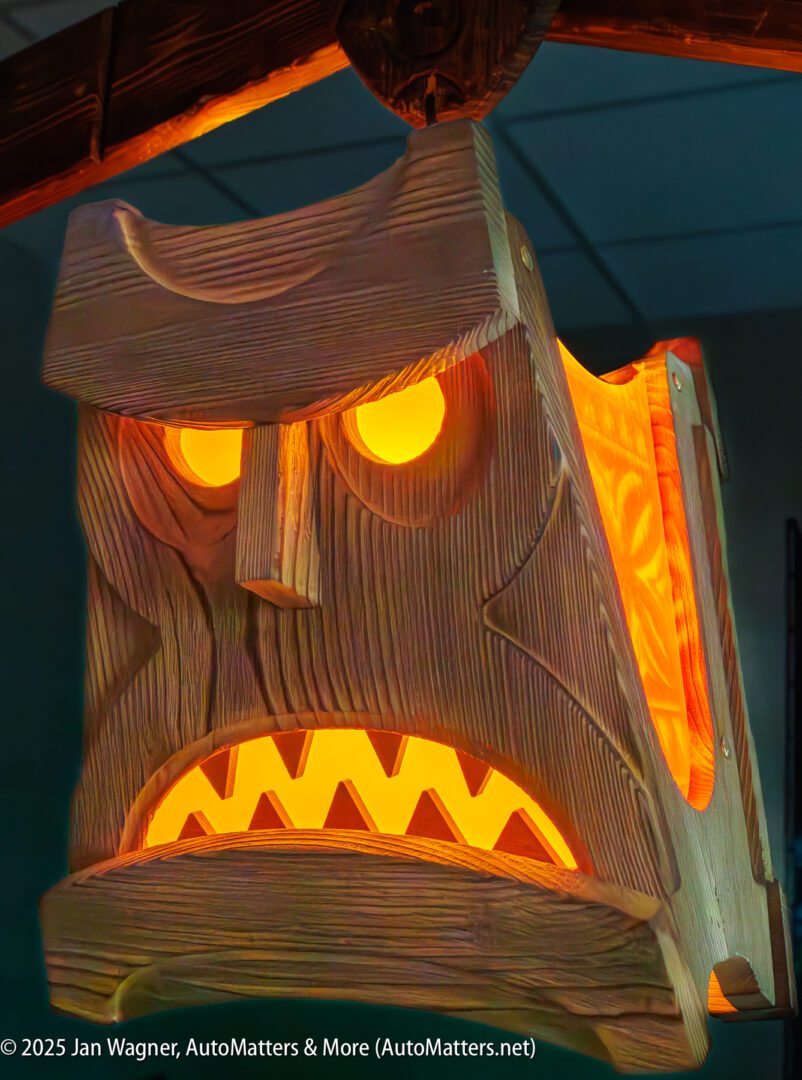 A wooden tiki-style lamp with a carved angry face is illuminated from within by orange-yellow light.