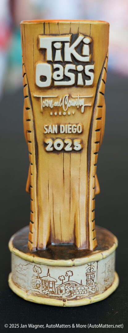 A tan ceramic mug with “Tiki Oasis Town and Country San Diego 2023” and a cityscape illustration at the base.