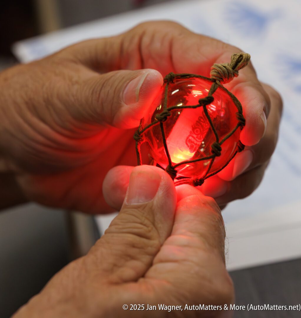 A person holds a glowing red glass fishing float wrapped in netting with both hands.