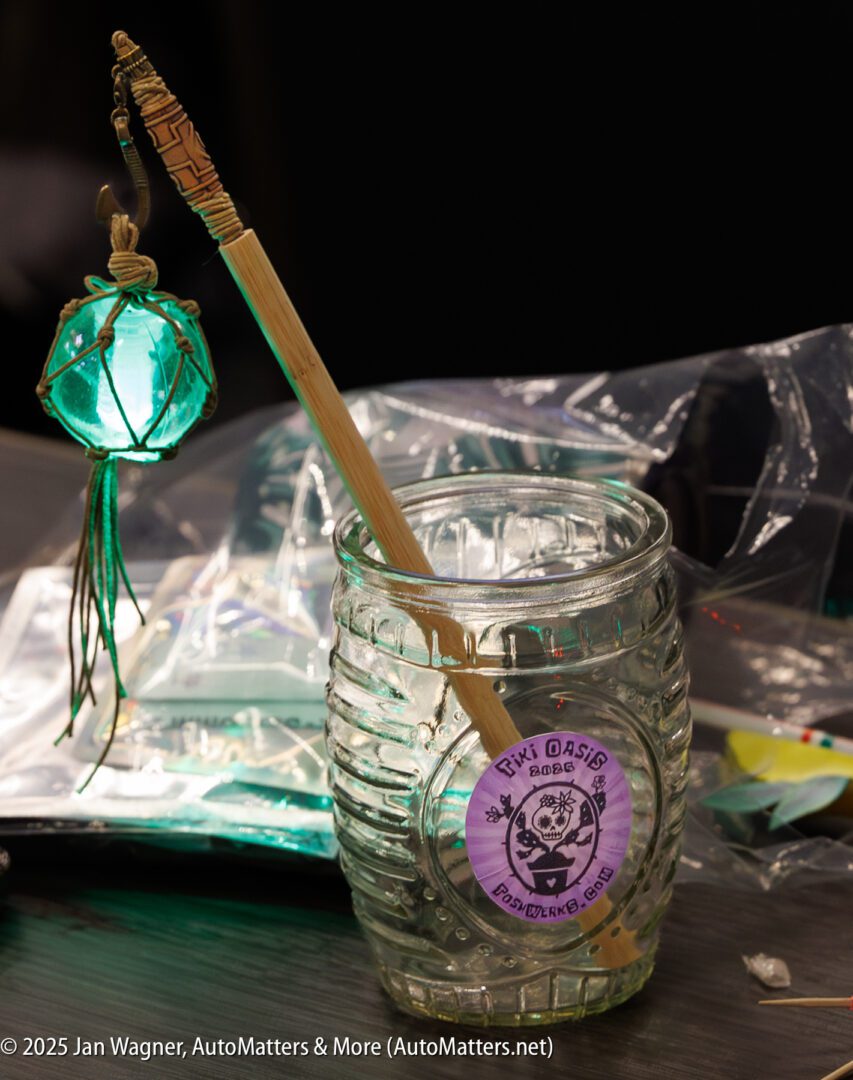 A glass jar labeled "PLYT OASIS" with a bamboo straw and a glowing green lantern decoration beside it sits on a table with plastic and paper items.