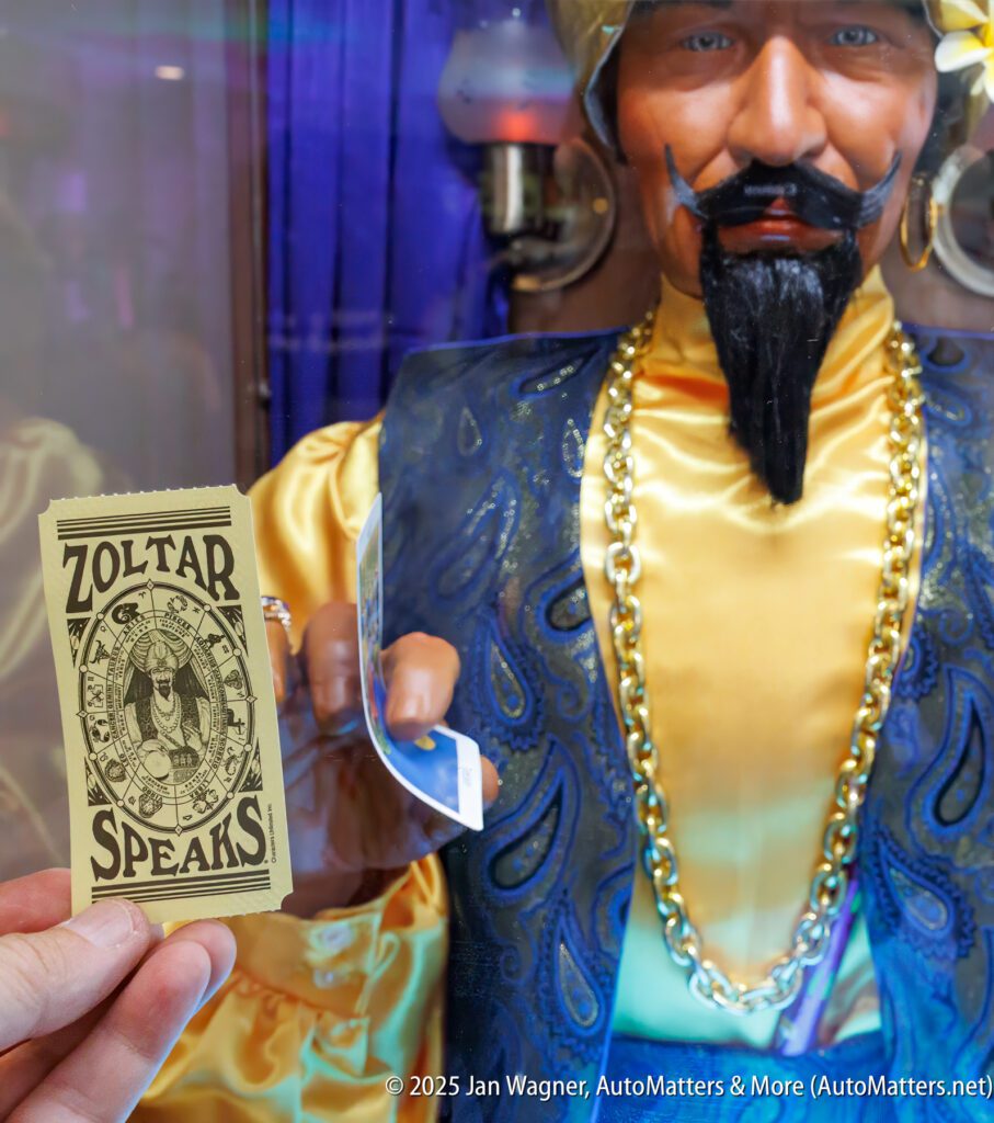 A close-up of a Zoltar fortune-telling machine with a person holding a "Zoltar Speaks" fortune card in front of the glass.
