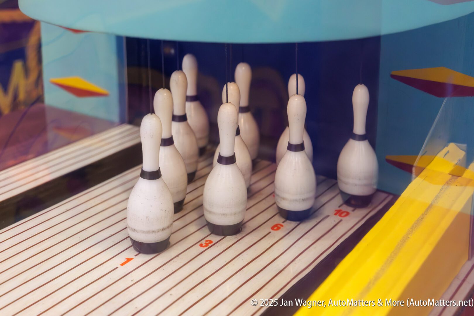 A close-up view of an arcade bowling game with ten white pins arranged in a triangular formation on a striped lane.