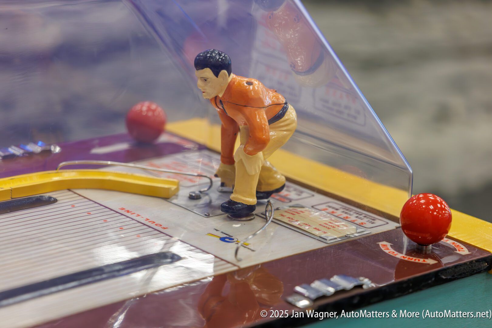 Close-up of a vintage tabletop baseball game featuring a plastic baseball player figurine and mechanical components under a clear cover.