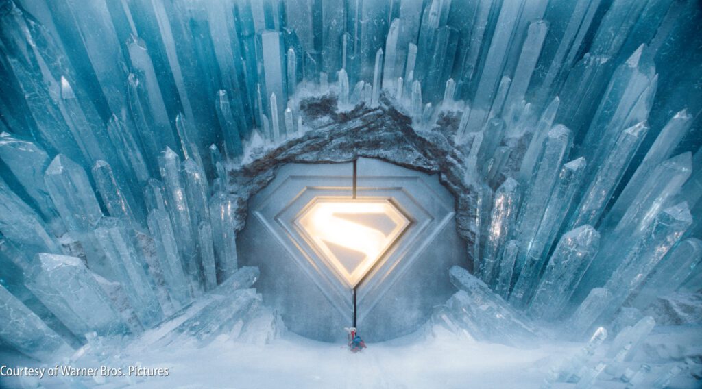 A person stands in front of a large, glowing Superman symbol embedded in an icy, crystal-covered wall.
