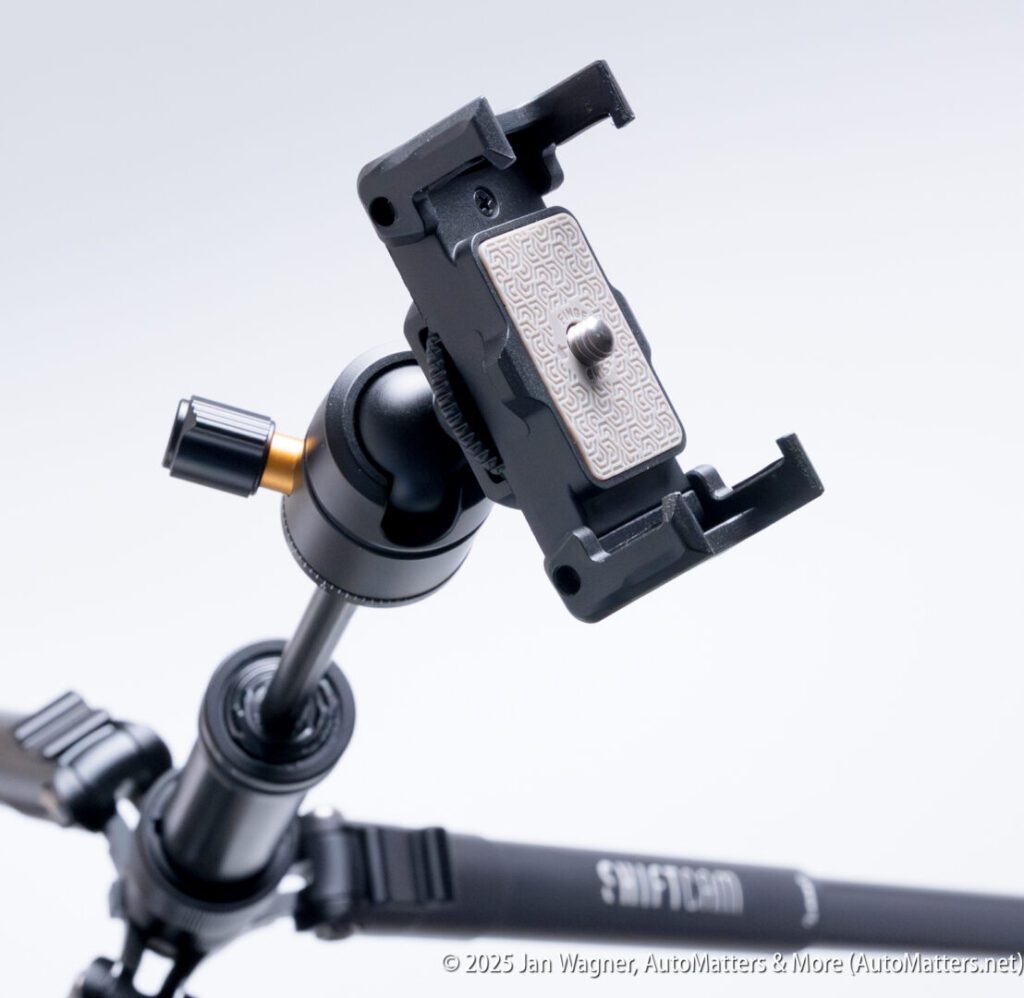 Close-up of a tripod head with a quick-release plate attached, showing adjustment knobs and part of the tripod legs.