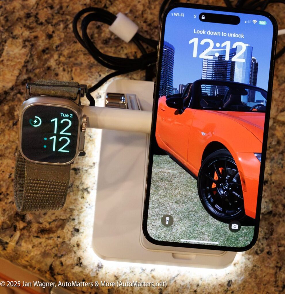 An Apple Watch and an iPhone on a white charging stand; the iPhone displays a red convertible car wallpaper and both devices show the time as 12:12.