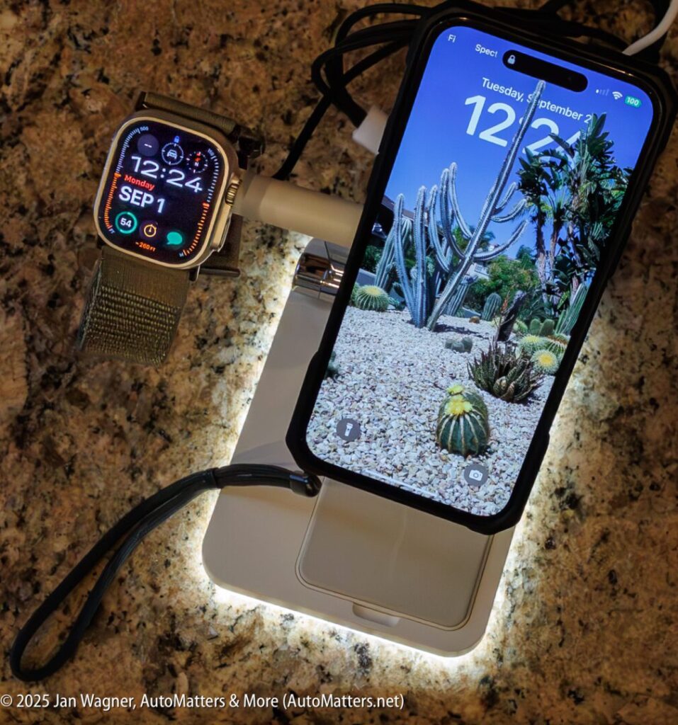 An Apple Watch and an iPhone are charging on a white wireless charging stand with a glowing base, placed on a granite countertop.