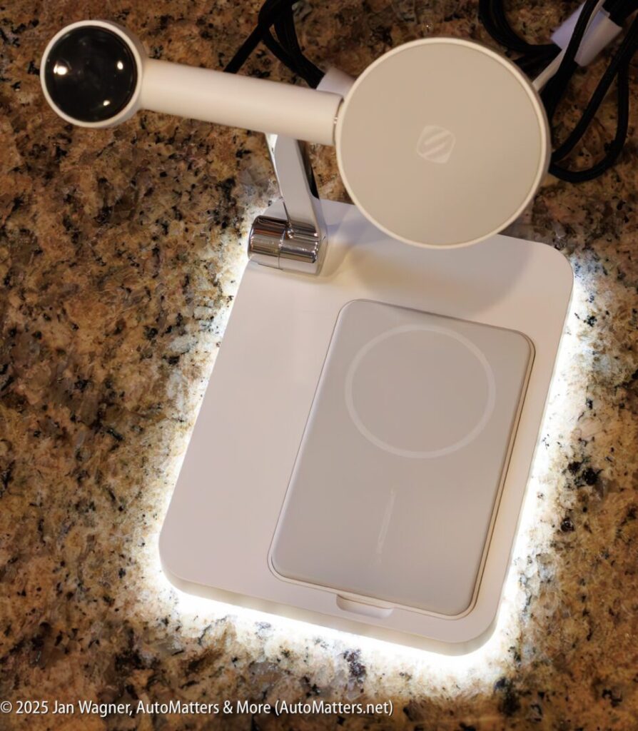 A white wireless charging stand with an adjustable arm and circular holder is placed on a granite countertop, illuminated by built-in LED lights.