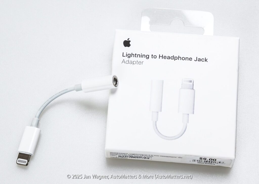 A Lightning to headphone jack adapter is shown next to its white retail packaging with Apple branding and product label.