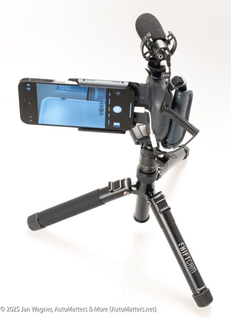 A smartphone mounted on a tripod with a microphone attached, displaying a camera interface on its screen.