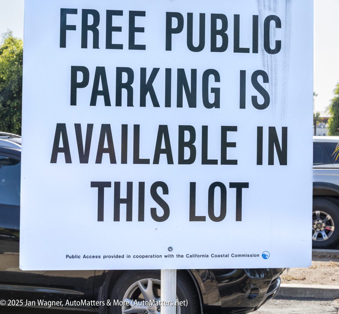 A sign reads "Free Public Parking Is Available In This Lot" with cars and trees visible in the background.